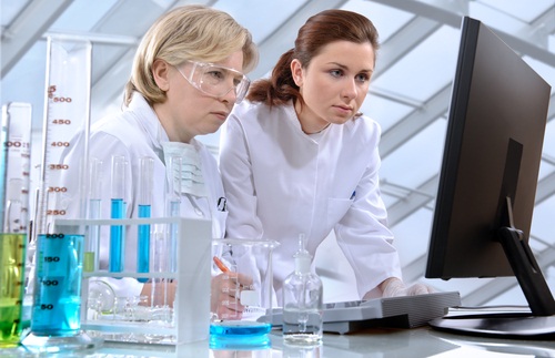 Pharmaceutical Rentals Two scientsists wearing labcoats look at a computer screen. Various chemicals in vials and beakers lay on the tbale next to them
