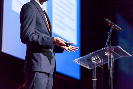 Product Release Event Rentals A speaker on a stage in front of a podium with a microphone