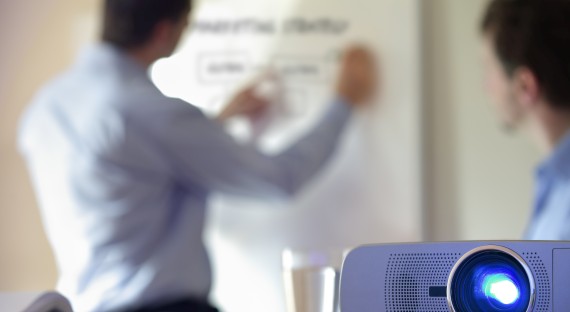 Trade Show Rentals Individuals working on a whiteboard while a projector in the foreground is shown illuminating